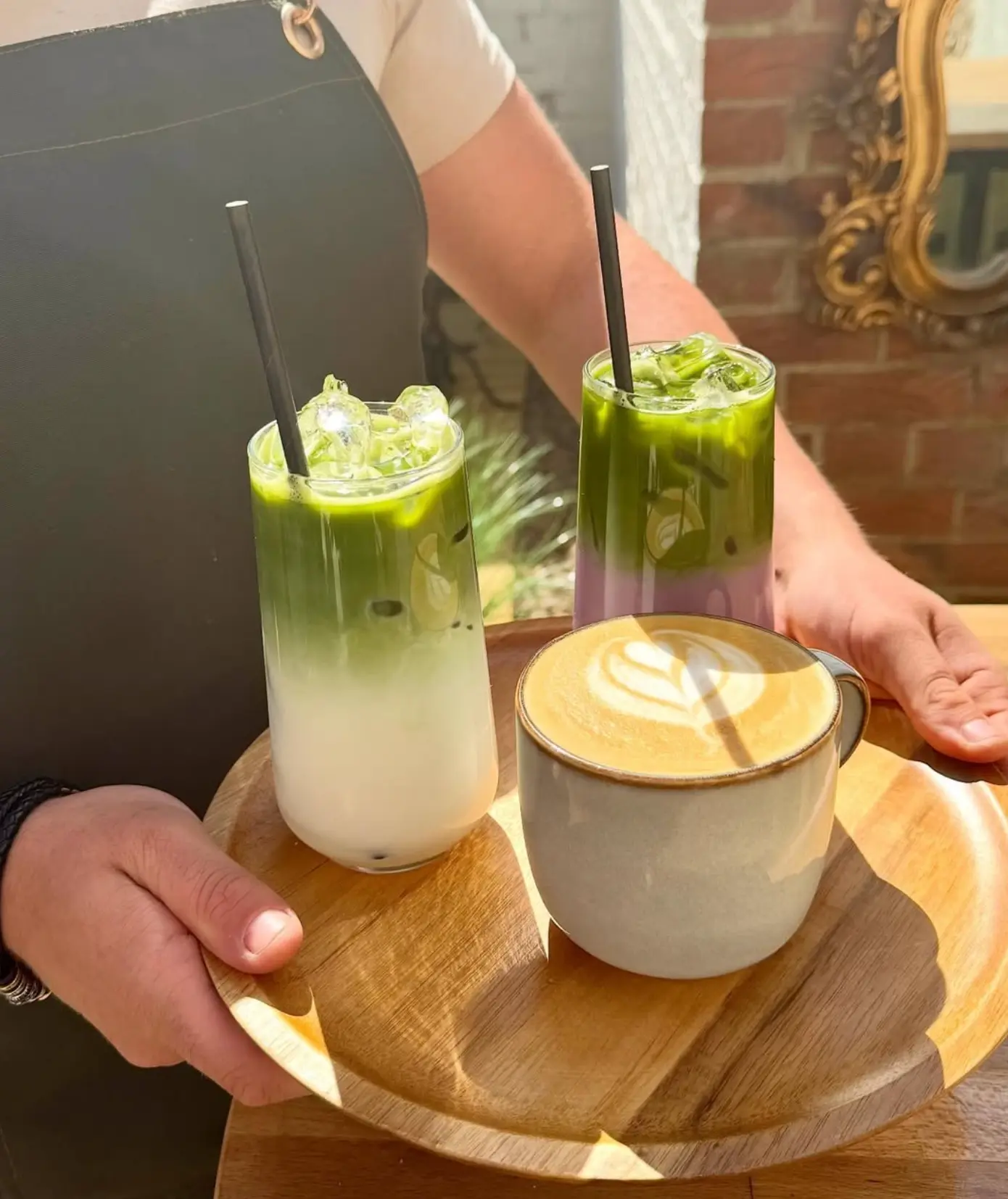 A member of the Leaf + Bean team carrying a wooden tray of iced matcha and a flat white